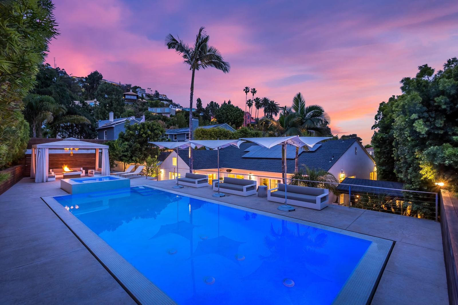 Infinity-edge pool overlooking the Hollywood Hills at sunset, palm silhouettes against a pink and purple sky