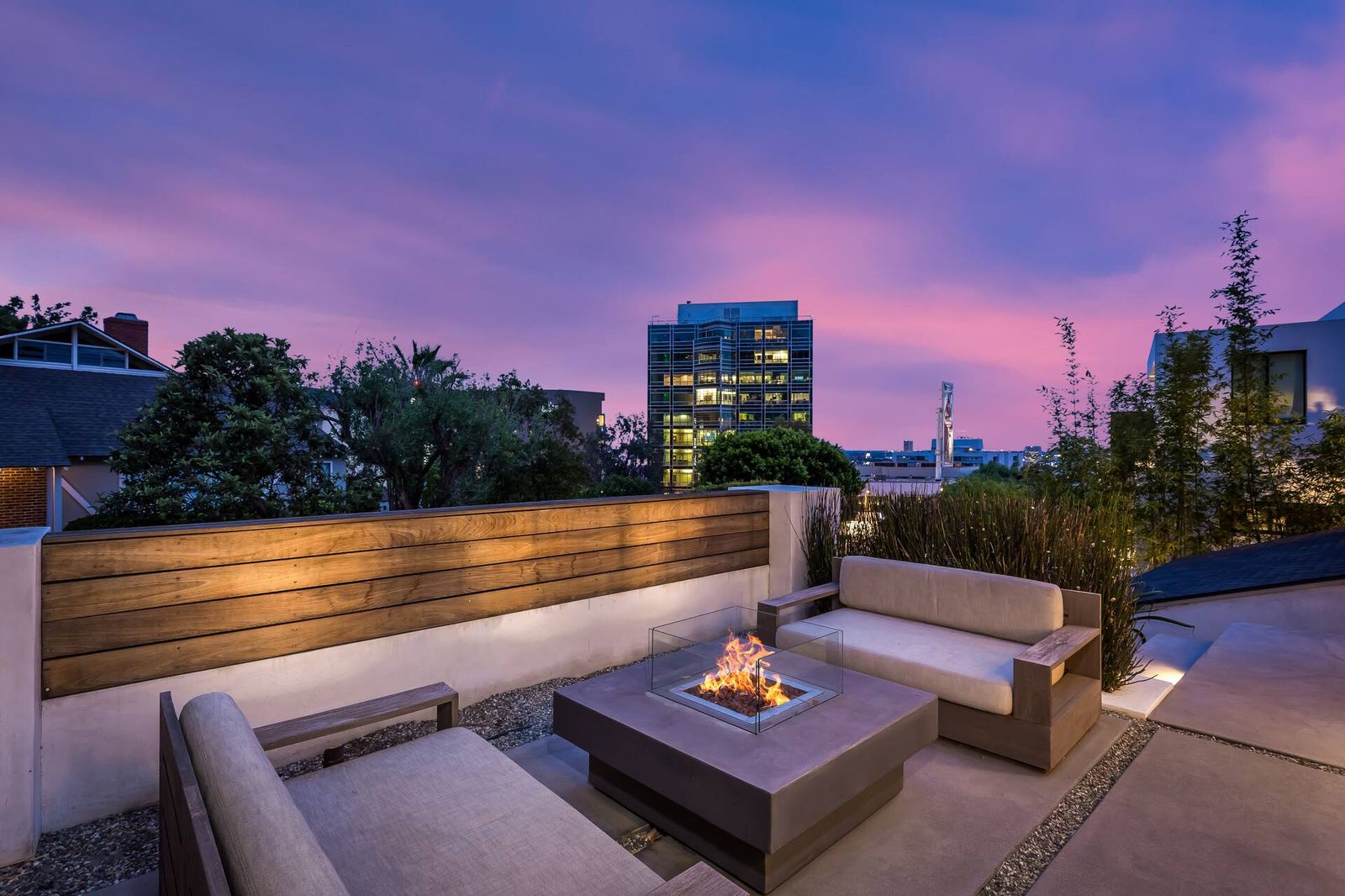 Rooftop patio with fire pit table and city skyline view at dusk